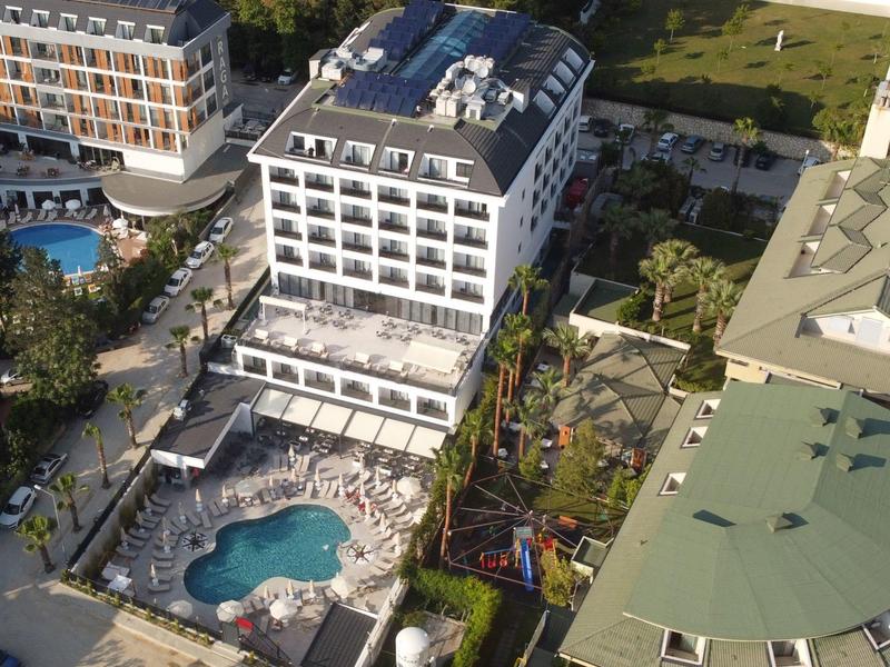 Aerial view of a hotel with pool, surrounding buildings, and green areas.