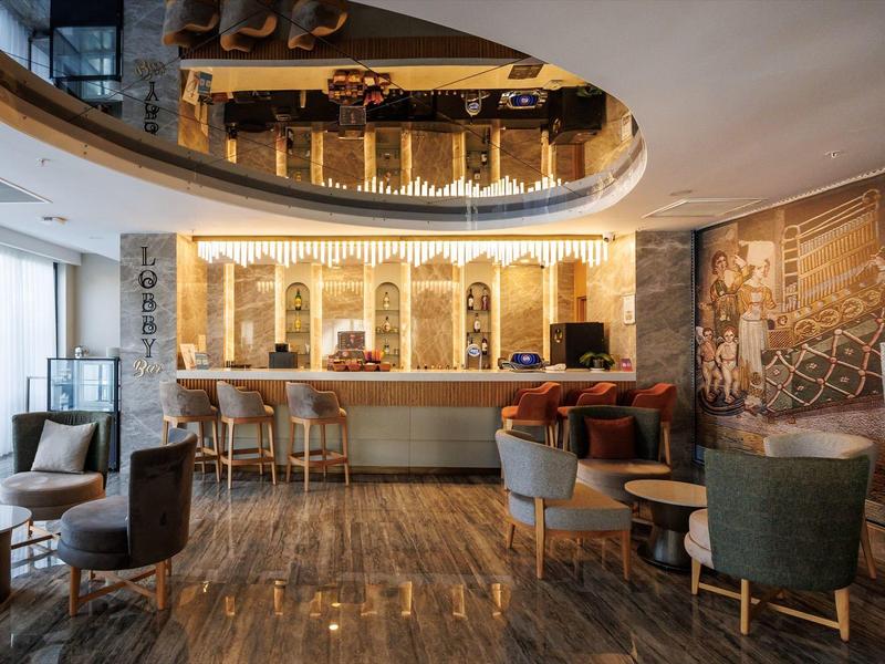 Modern hotel bar with seating, wooden floor, and decorative ceiling.