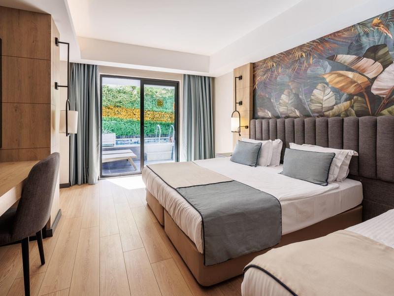 Modern hotel room with double bed, desk, and balcony access overlooking nature.