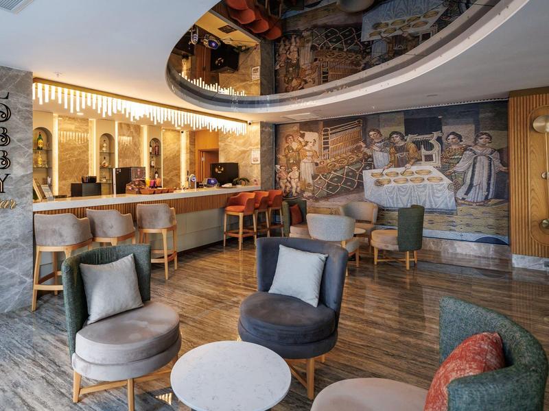 Modern hotel lounge seating area with round chairs, bar, and large wall mural.