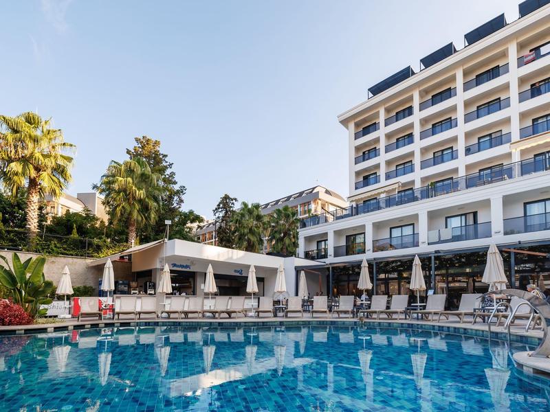 Modern hotel pool area with lounge chairs and umbrellas on a sunny day.