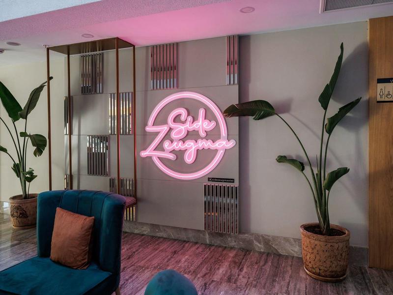 Modern hotel lounge with pink neon sign and green potted plants.