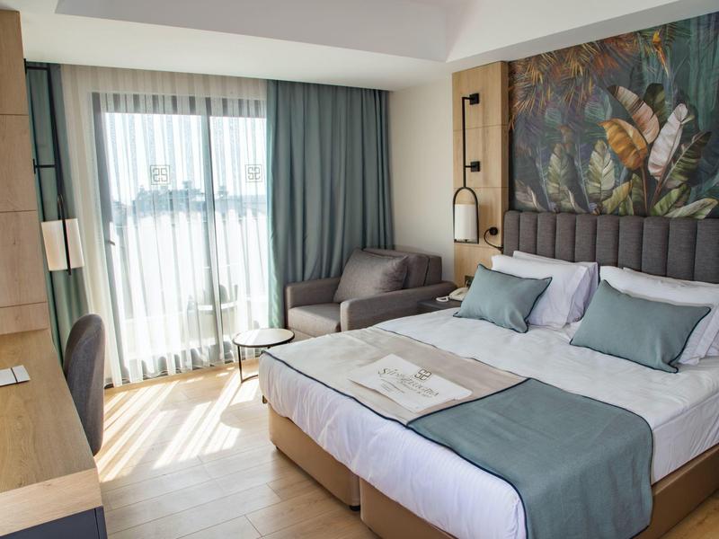 Modern hotel room with double bed, seating area, and large window with curtains.