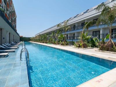 Long outdoor pool beside hotel rooms with lounge chairs and palm trees under clear sky.