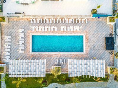 Aerial view of a rectangular pool with sun loungers and umbrellas in a hotel garden.