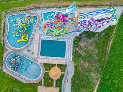 Luchtfoto van een waterpark met zwembaden, glijbanen en omliggend parkgebied.