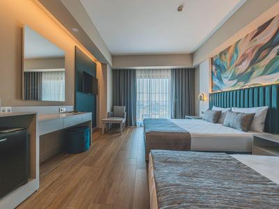 Moderne hotelkamer met bed, bureau, tv en groot raam met gordijnen.