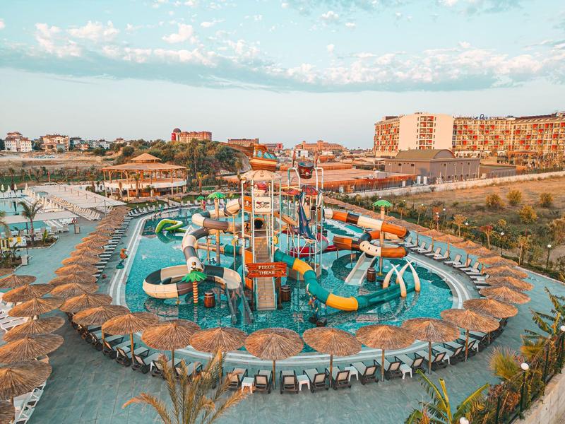 Waterpark met glijbanen en parasols vlakbij een hotel en strand.