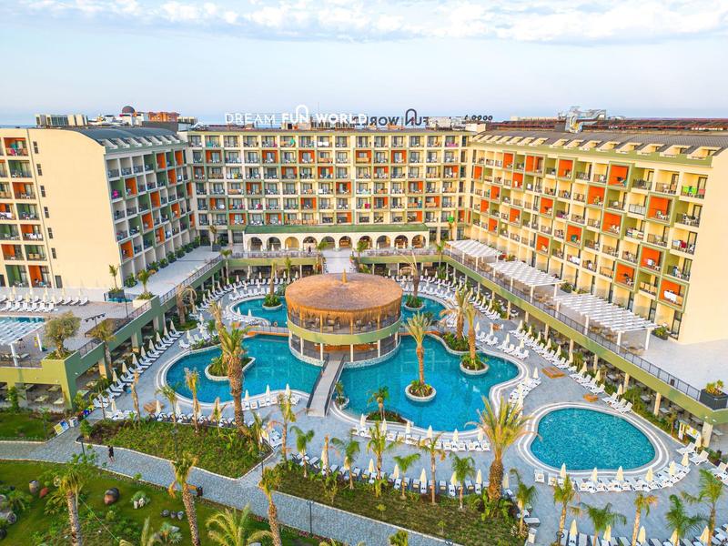 Groot hotel met meerdere zwembaden en ligstoelen buiten.