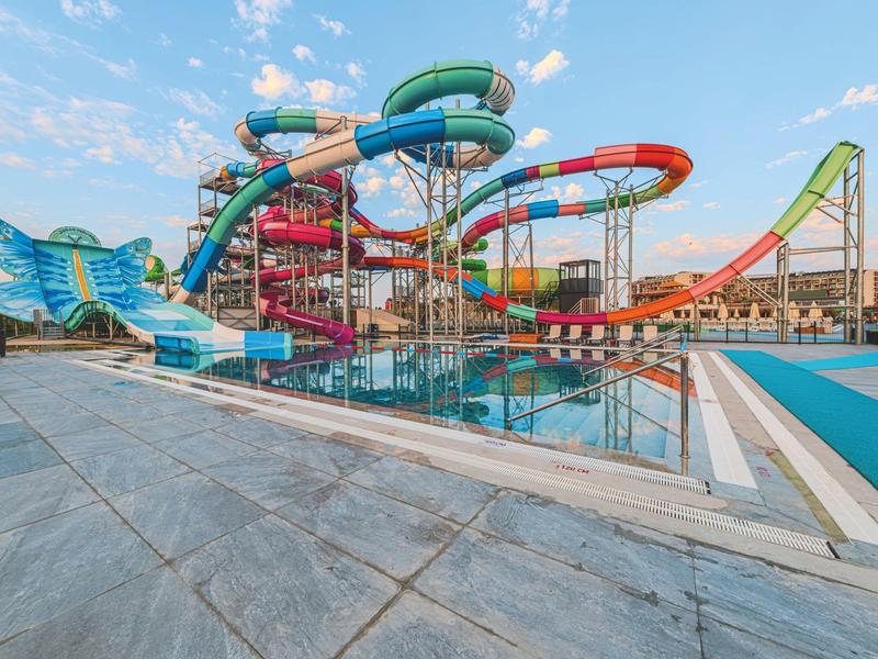 Kleurrijk waterglijbaan- en zwembadcomplex onder een heldere hemel bij een vakantiepark.