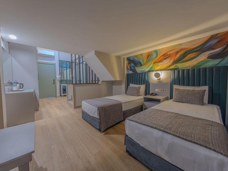 Modern ingerichte tweepersoonskamer met twee bedden en kleurrijk kunstwerk boven het hoofdeinde.