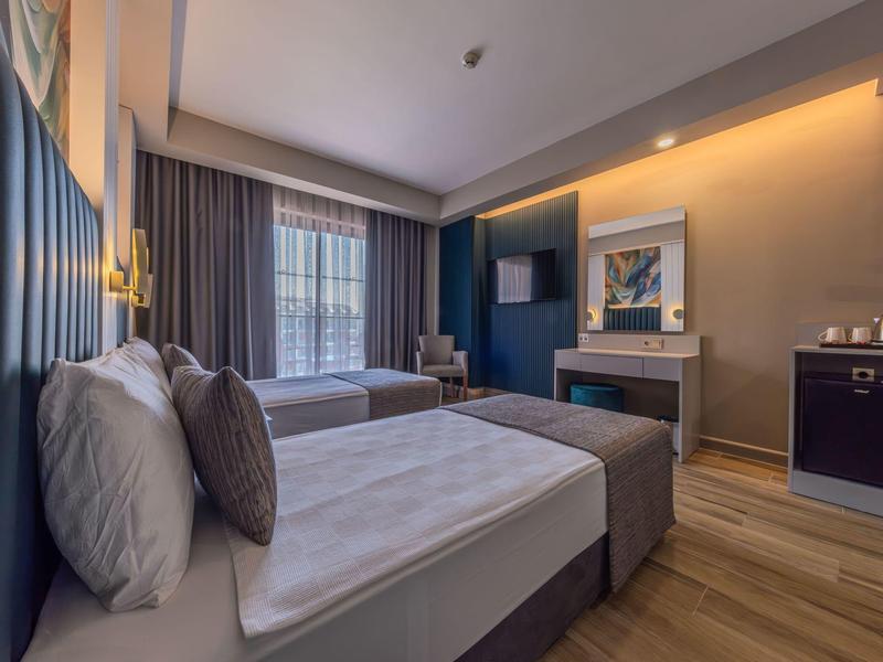 Modern hotelkamer met twee bedden, bureau en groot raam met gordijnen.