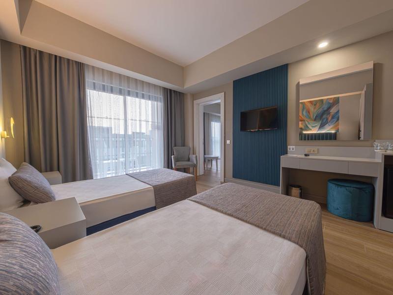 Modern hotelkamer met twee bedden, bureau en groot raam met gordijnen.