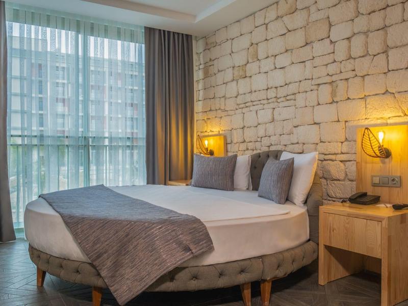 Moderne hotelkamer met rond bed, stenen muur, groot raam en zachte gordijnen.