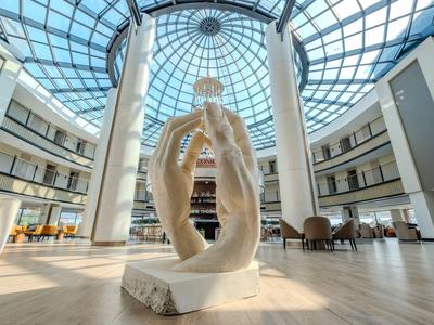 Nowoczesna lobby hotelowa z dużą szklaną kopułą i wysoką rzeźbą rąk w centrum.