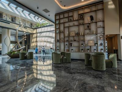 Hotel-Lobby mit Marmorboden, grünen Sesseln und großer Wand mit dekorativen Objekten.