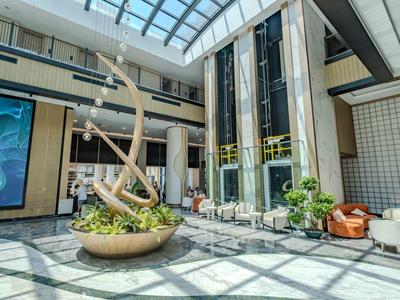 Heller, moderner Hotellobby mit Sitzbereichen und großer Skulptur unter Glasdach.