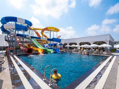 Großer Pool mit bunten Wasserrutschen und Liegestühlen unter blauem Himmel.