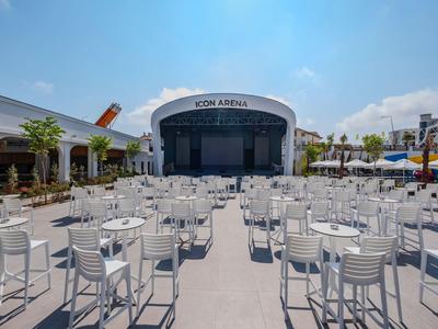 Scena na świeżym powietrzu z wieloma białymi krzesłami i stołami pod niebieskim niebem.