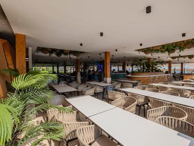 Große überdachte Terrasse mit weißen Tischen und Stühlen in einem Hotelrestaurant.