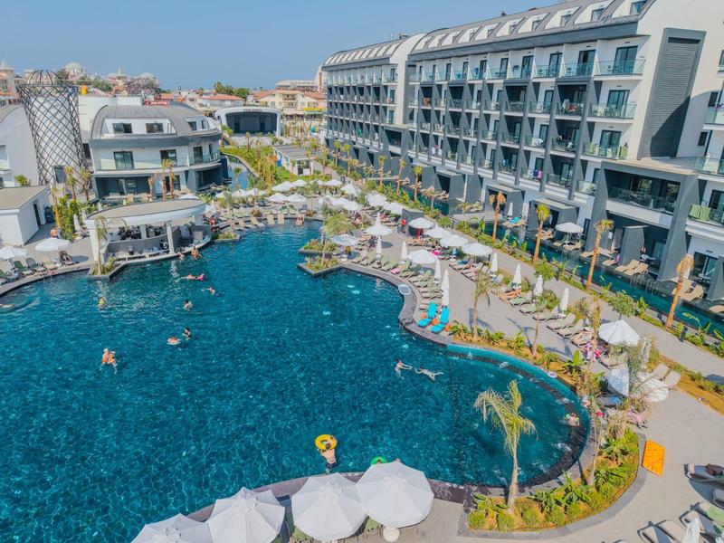 Großes Hotel mit Außenpool und Liegestühlen an einem sonnigen Tag.