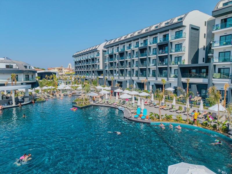 Großes Hotel mit Pool, Sonnenliegen und Menschen, die im Wasser entspannen.