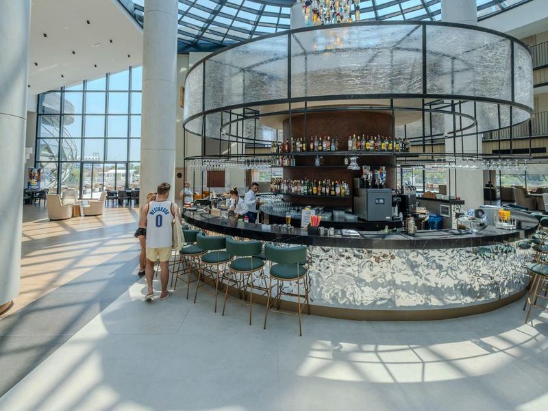 Moderner Hotelbarbereich mit runden Tresen und vielen Sitzplätzen, umgeben von großen Fenstern.