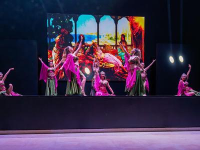 Tanečníci v růžových kostýmech předvádějí živou scénickou show s barevným pozadím.