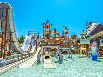 Großer Wasserpark mit vielen bunten Wasserrutschen, Becken und spielerischen Figuren unter klarem blauen Himmel.