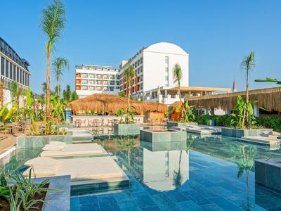 Moderner Hotelpool mit Palmen, Liegen und klar blauem Wasser unter hellem Himmel.