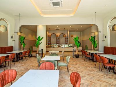 Heller, moderner Gastraum mit roten Stühlen, weißen Tischen, Pflanzen und großen Bogenfenstern.