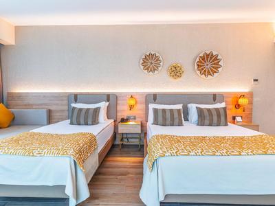 Světý hotelový pokoj se dvěma postelemi, žlutými akcenty a dekorativními nástěnnými ozdobami.