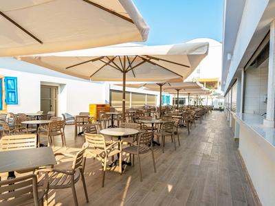 Velká terasa s stoly a židlemi pod slunečníky u hotelu.