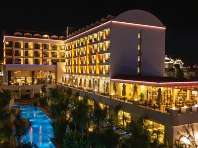 Moderní hotel v noci s osvětleným bazénem a teplým osvětlením v pokojích.