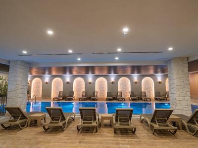 Moderner Indoor-Pool mit blauen Wasser, Liegestühlen in Reihe und runden Wandnischen mit Beleuchtung.