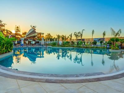 Velký kulatý bazén s čistou vodou obklopený palmami a slunečníky při západu slunce.