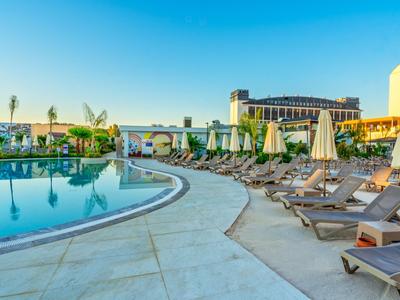 Bazén s lehátky a slunečníky před hotelovou budovou pod jasnou oblohou.