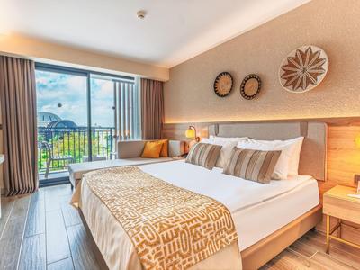 Moderně zařízený hotelový pokoj s velkou postelí, posezením a balkonem s výhledem na zahradu.