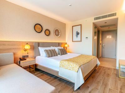 Moderní hotelový pokoj s postelí, pohovkou a teplým osvětlením v světlých tónech.