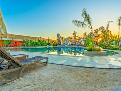 Oblast bazénu s lehátky, slunečníkem a rostlinami při západu slunce.