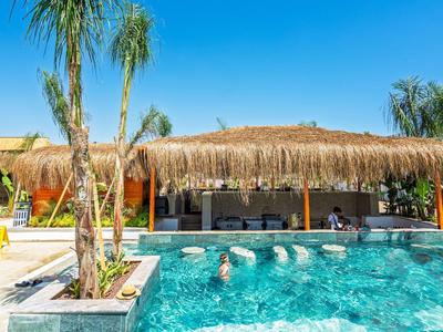 Moderner Pool mit Palmen, Strohdachbar und blauem Wasser unter klarem Himmel.