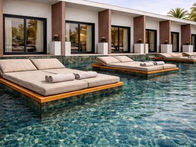 Velká lehátka v bazénu před moderními hotelovými pokoji s palmami v pozadí.