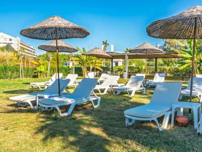 Bílé lehátka a slunečníky na zelené trávě pod jasnou oblohou.