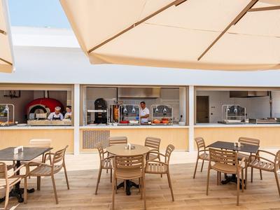 Terrasse mit Holztischen, Stühlen und großen Sonnenschirmen vor einem Café mit offenem Schalter.