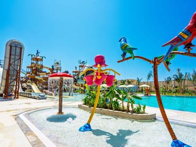 Barevný vodní park s sochami ptáků a skluzavkami pod jasně modrou oblohou.