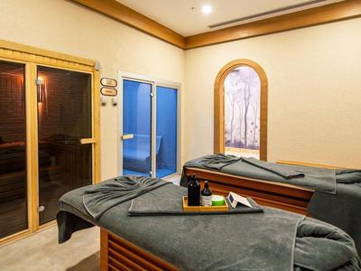 Ein heller Wellnessraum mit zwei Massageliegen, blauen Handtüchern und einem kleinen Fenster.