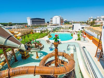 Vodní park se skluzavkami a bazénem před hotelovými budovami za slunečného počasí.