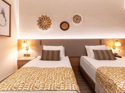 Hotelový pokoj s dvěma jednolůžky, nočními stolky a moderními dekoracemi na stěně v teplých odstínech.