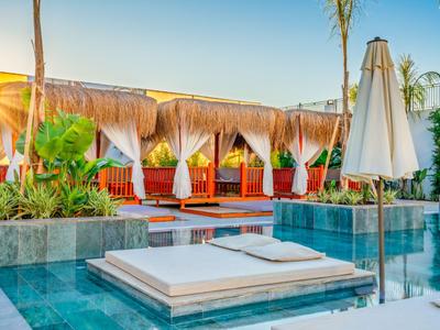 Luxusní bazénová oblast s lehátky a slunečníky v hotelovém resortu při západu slunce.