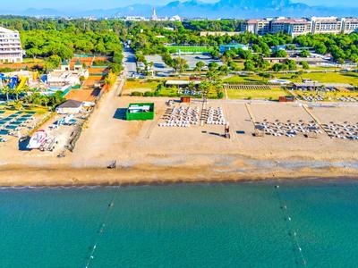 Široká písečná pláž s deštníky, lehátky a hotely v pozadí u moře